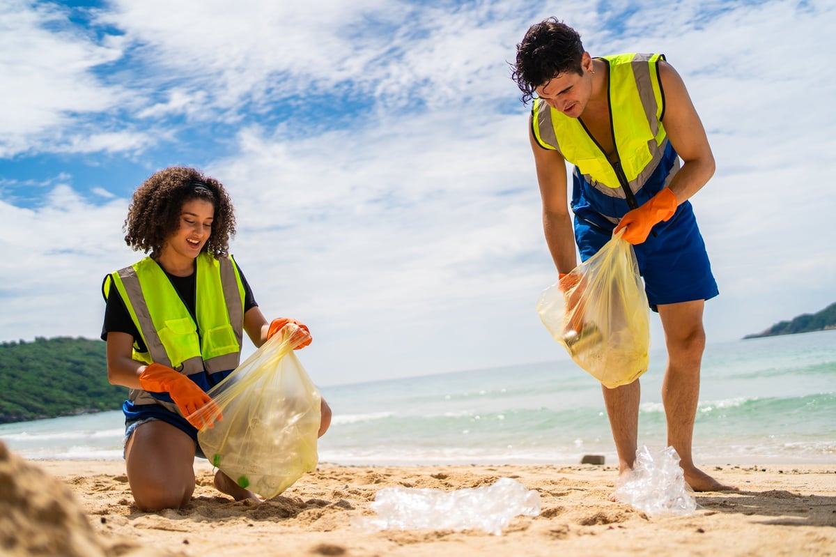 Two volunteers collecting plastic bottles and trash on a sandy beach
